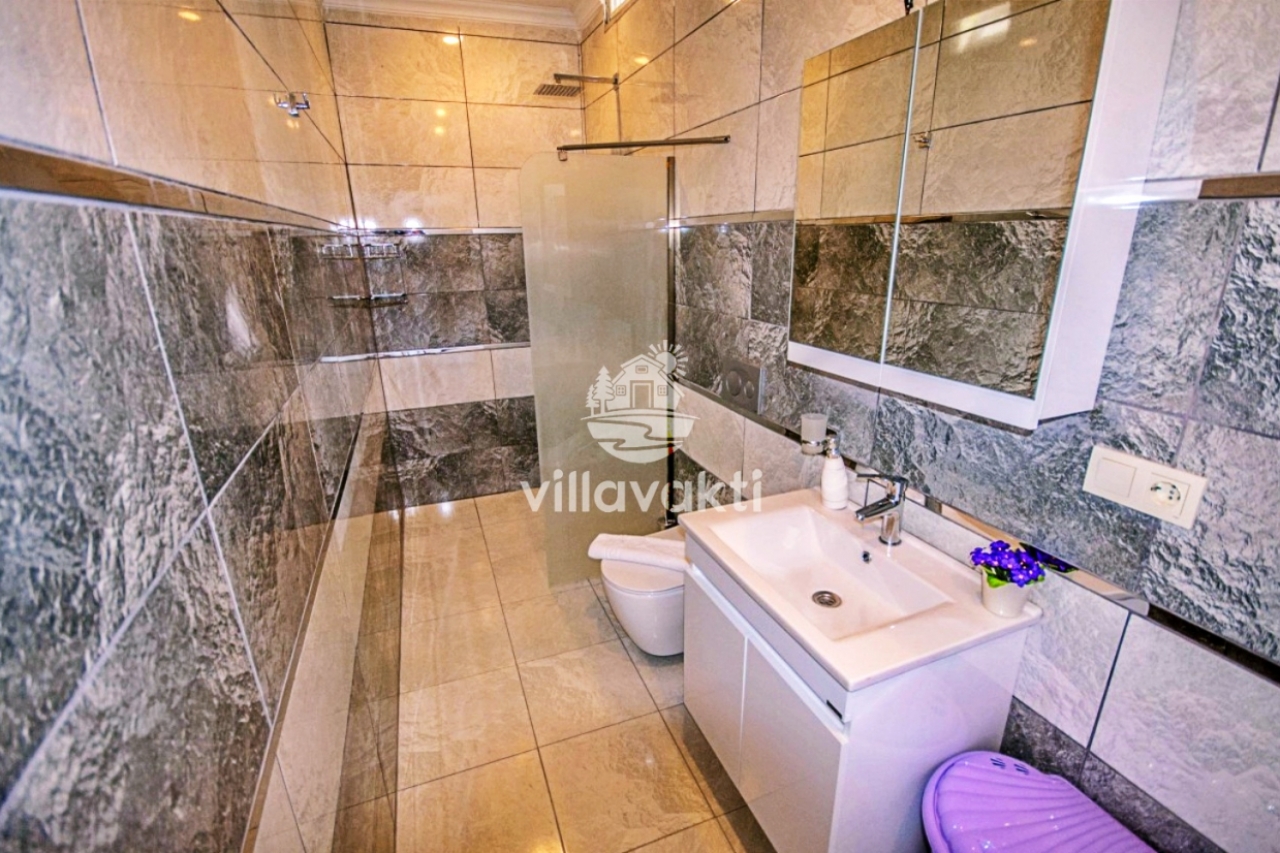 Gri mermer kaplı duvarları olan modern banyoda duşakabin ve lavabo.
