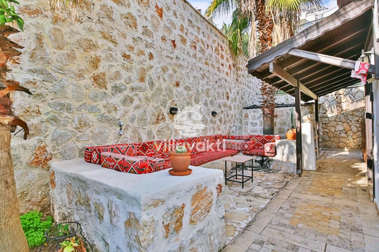 Taş duvar önünde kırmızı desenli minderli oturma alanı ve ahşap pergola.