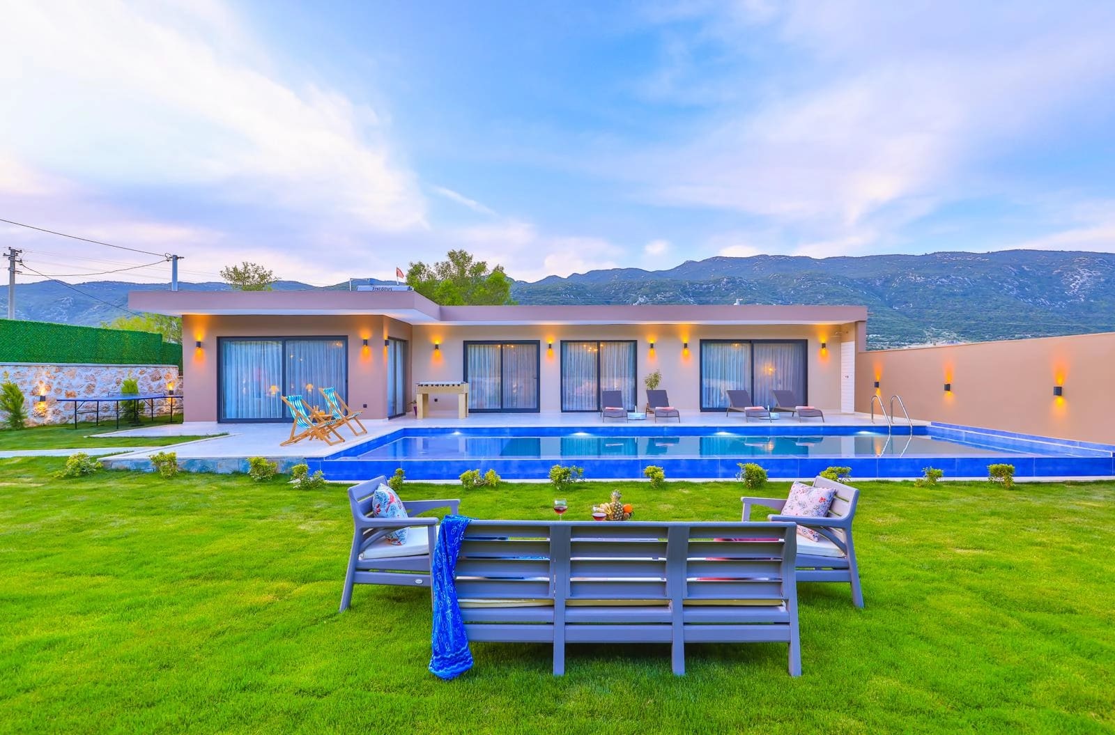 Önünde havuz ve çim alan bulunan tek katlı modern villa.